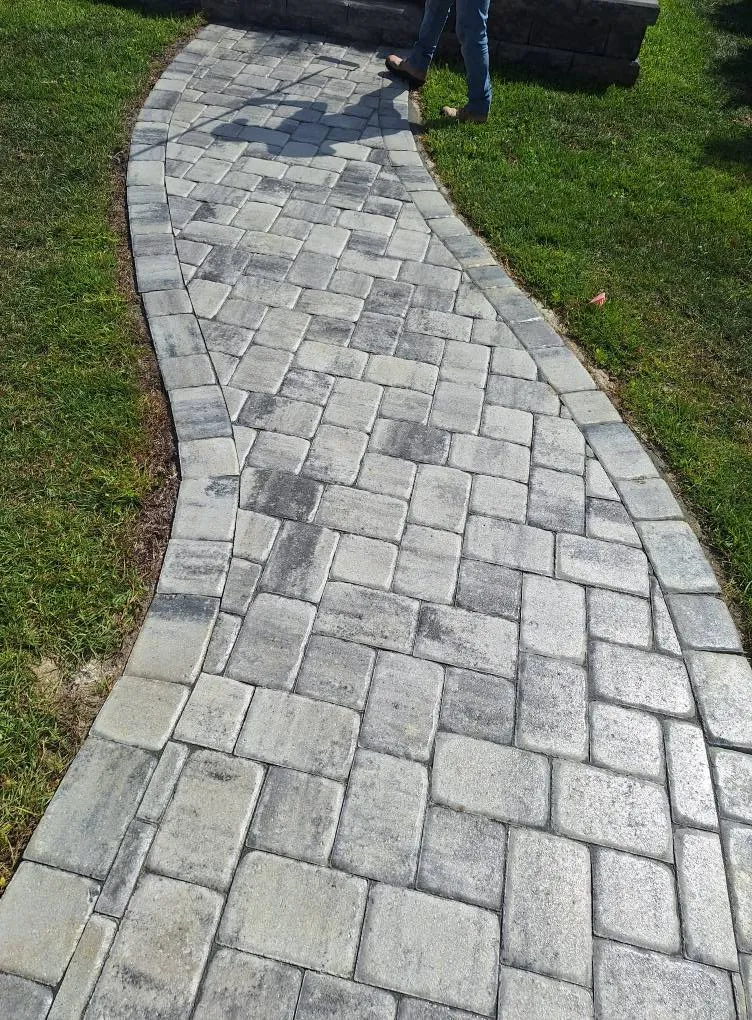 Curved gray paver walkway bordered by grass