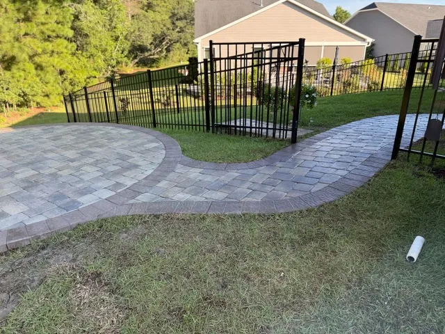 Paver walkway curving through a landscaped yard with metal fencing